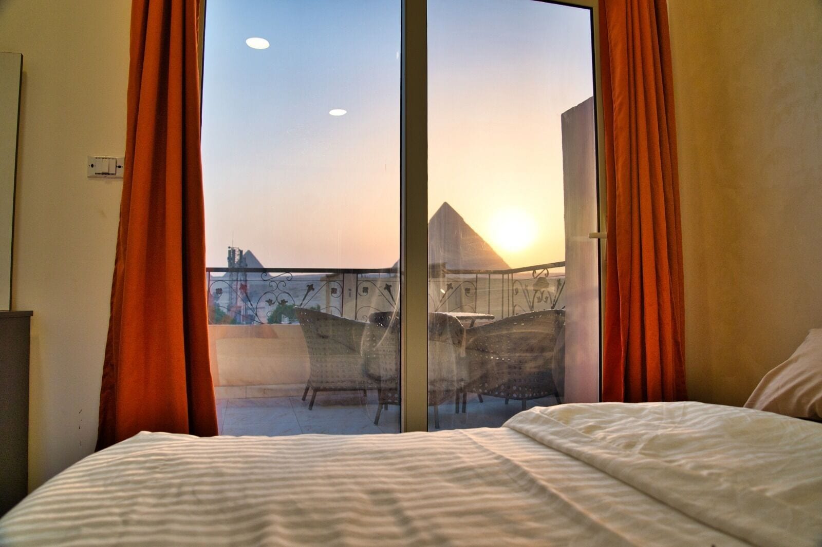 Een hotelkamer met een grote schuifdeur naar een balkon met uitzicht op een stadsgezicht en een piramide.