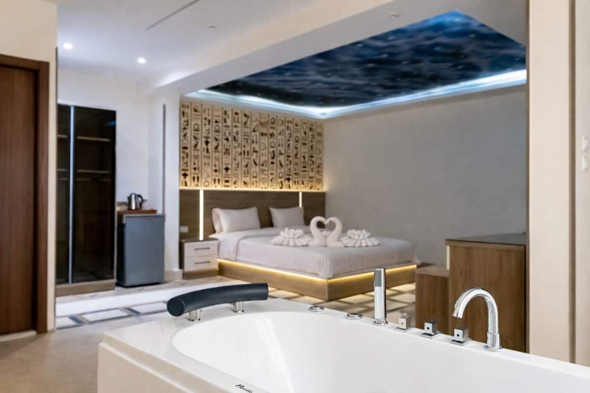 Une chambre à coucher moderne comprenant un lit, une table de chevet, une armoire intégrée et une salle de bain avec une baignoire et un lavabo.