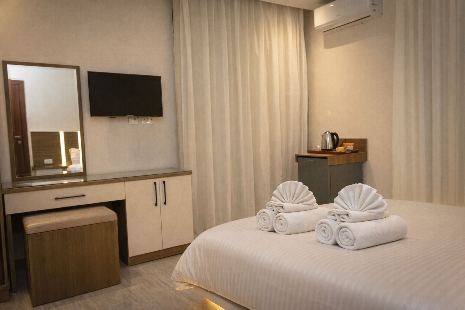Een hotelkamer met een bed, een bureau, een spiegel, een televisie en een klein keukenblok.