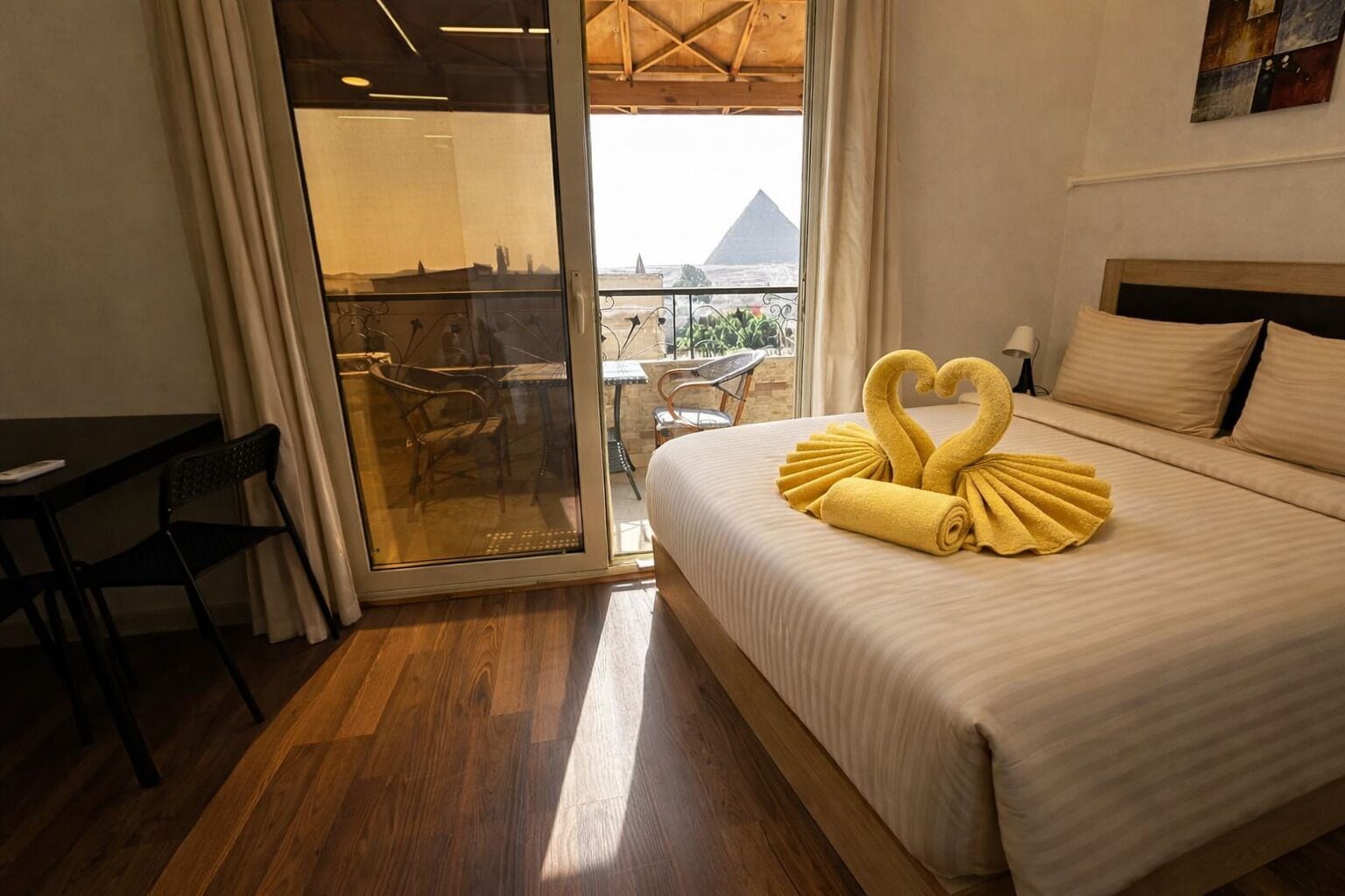 A hotel room with a bed, a desk, and a view of a pyramid through a glass door.
