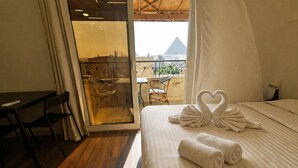 A hotel room with a bed, a desk, and a view of a pyramid through a glass door. - Narmer Pyramids View (Giza)