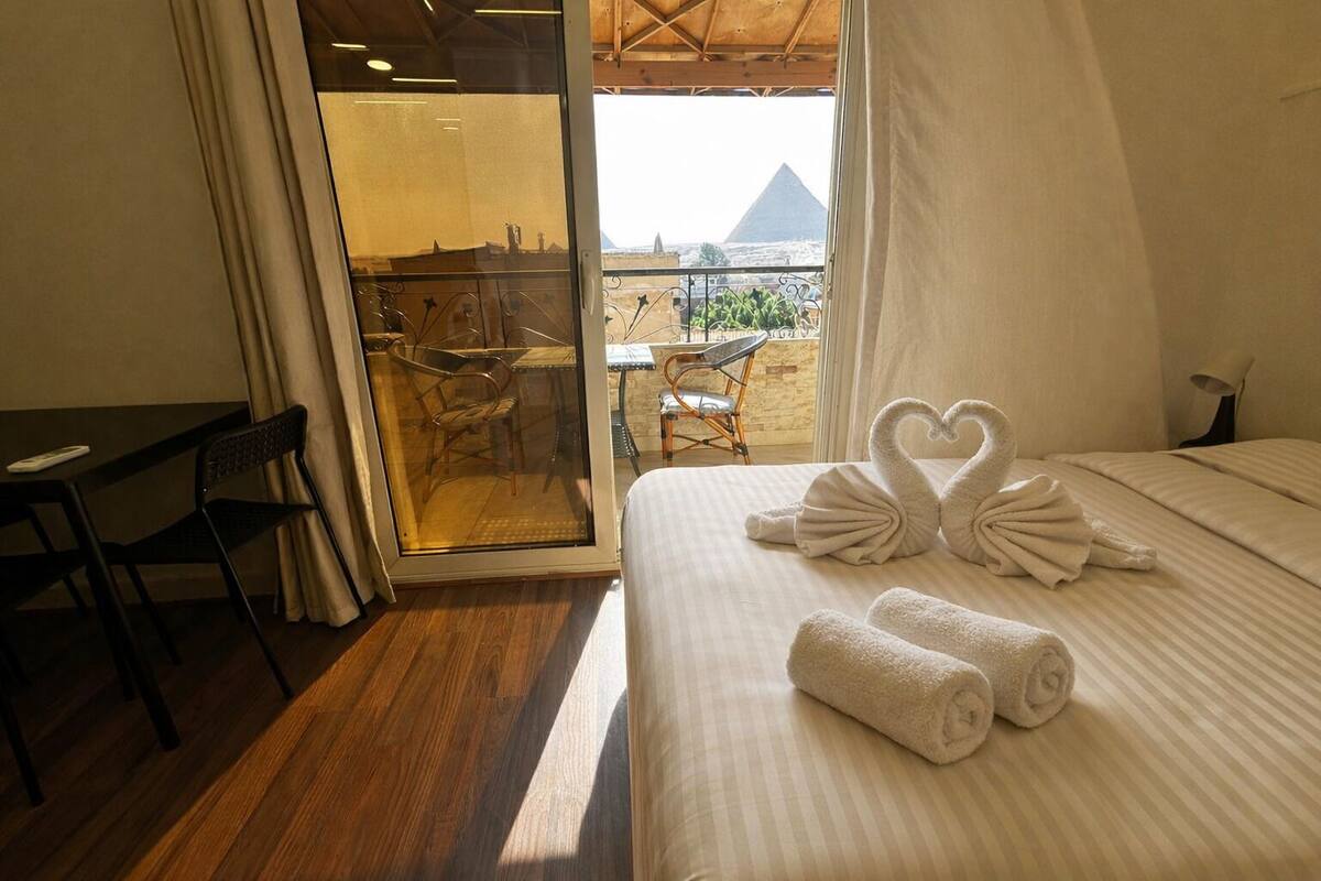 Une chambre d’hôtel avec un lit, un bureau et une vue sur une pyramide, visible à travers une porte vitrée.