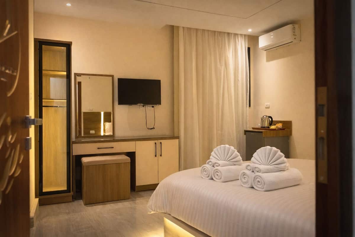 Une chambre d’hôtel équipée d’un lit, d’un bureau, d’un miroir, d’une télévision et d’un mini-bar.