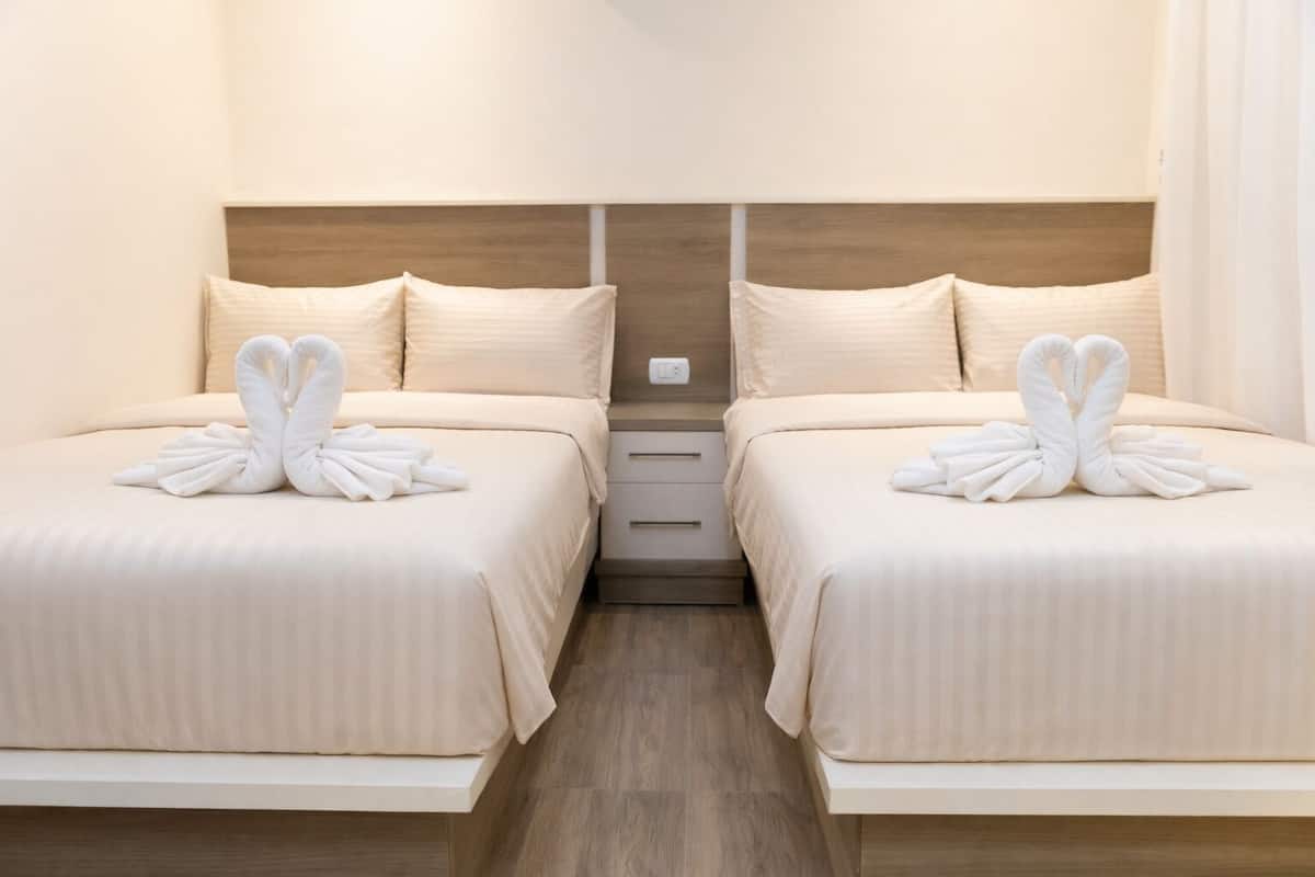 Une chambre d’hôtel avec deux lits, chacun doté d’une tête de lit et agrémenté d’une paire de serviettes disposées en forme de cœur.