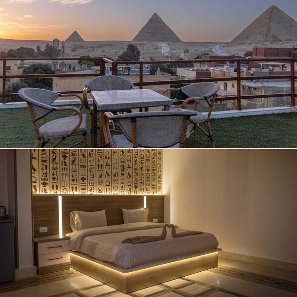 A balcony with a view of pyramids, a bed with a headboard featuring hieroglyphs, and a nightstand. - Narmer Pyramids View (Giza)