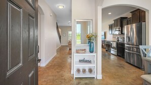 Una cucina moderna con elettrodomestici in acciaio inossidabile, un tavolo consolle bianco con la scritta 'welcome' e vista sull'area pranzo.