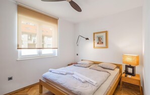 Ein Schlafzimmer mit Bett, Nachttisch mit Lampe, Fenster mit Jalousien und einem gerahmten Bild an der Wand.