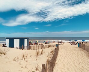 A beach with a wooden fence, beach umbrellas, and a small blue and white building.
