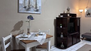 A dining area with a table set for two, a vase with a single flower, and a painting above the table.