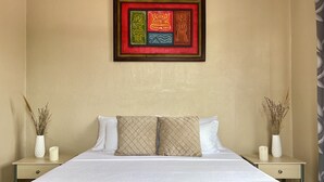 A neatly made bed with white linens and two decorative pillows, a framed artwork above the bed, and two bedside tables with vases and candles.