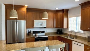 Eine moderne Küche mit Holzausstattung, Edelstahlgeräten, Granit Arbeitsplatten und Pendelleuchten.