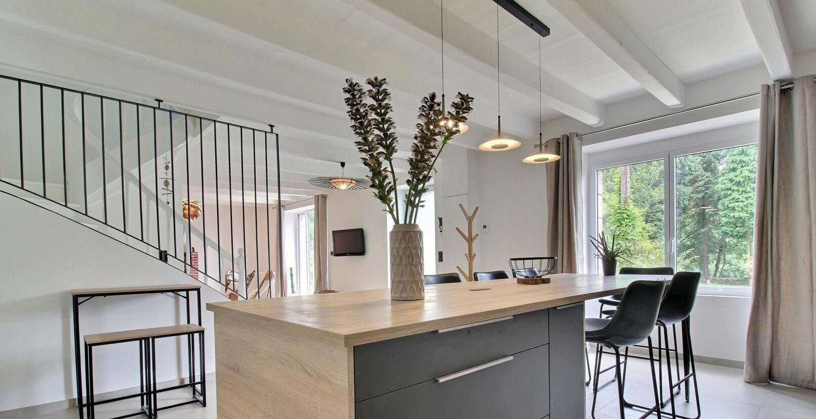 Une cuisine moderne avec un îlot central en bois, des chaises noires et des luminaires suspendus.