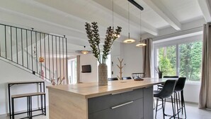 A modern kitchen with a wooden island, black chairs, and pendant lights.