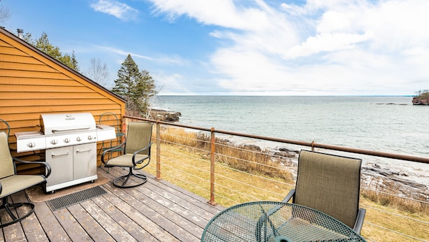 En terrass med grill, stolar och utsikt över havet.