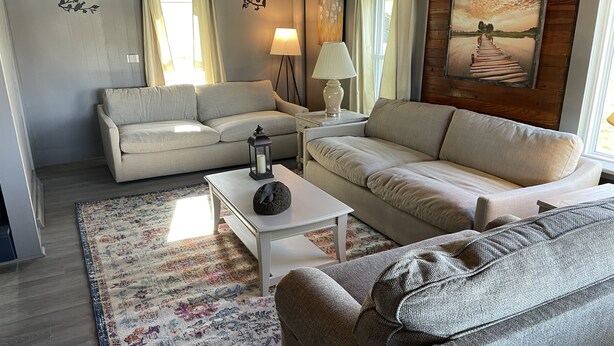 A living room with a sofa, a coffee table with a decorative item, a lamp, and a rug. -  Lakefront Farmhouse with 2 acres to enjoy -  Fish, Kayak, or launch your boat! (Cochranton)