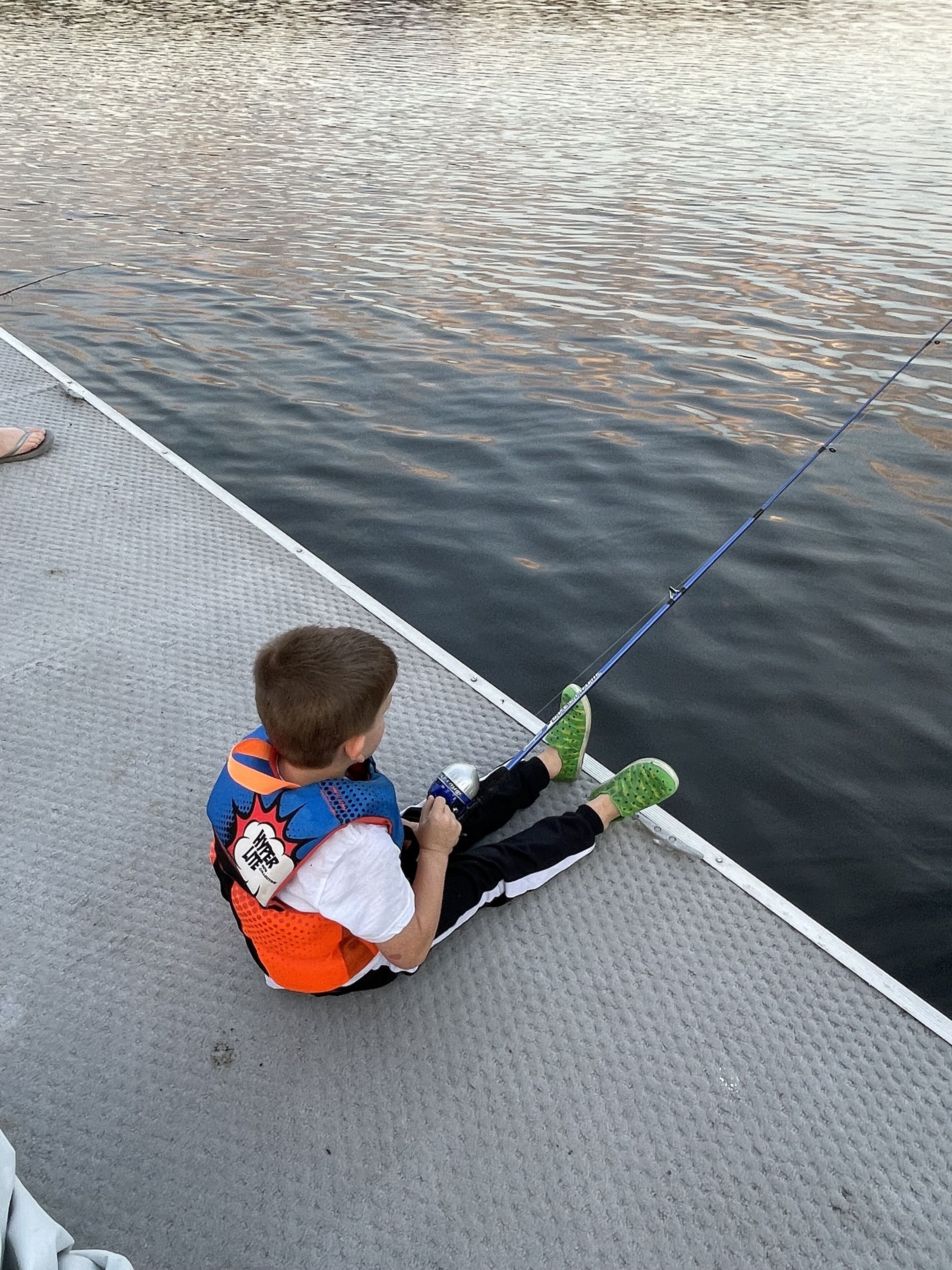 Un enfant est assis sur un quai, tenant une canne à pêche.