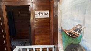 A wooden interior with a crib, a welcome sign, and a painting of a boat. -  Lakefront Farmhouse with 2 acres to enjoy -  Fish, Kayak, or launch your boat! (Cochranton)