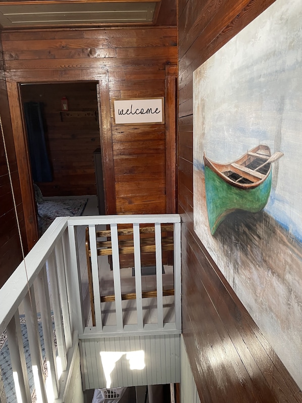 A wooden interior with a crib, a welcome sign, and a painting of a boat.