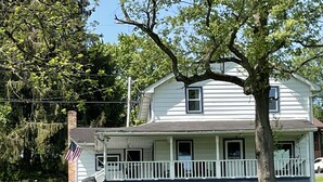 A two-story house with a front porch, a garage, and a large tree in front. -  Lakefront Farmhouse with 2 acres to enjoy -  Fish, Kayak, or launch your boat! (Cochranton)