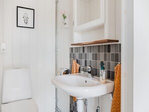 A bathroom with a white sink, a mirror, a framed artwork, and a small vase with flowers. - Flugebacken by Interhome (Sandhem)