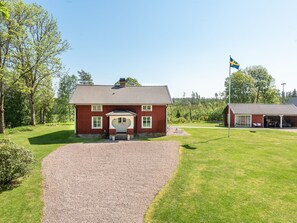 A red wooden house with a gravel driveway and a flagpole with a flag. - Flugebacken by Interhome (Sandhem)
