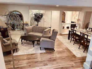 A living room with a sofa, armchair, coffee table, and dining area with chairs and a table. - FireThorn Manor: Spacious, well appointed 2 Bedroom Garden Suite with King Bed. (North Saanich)