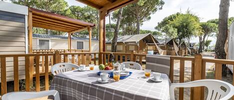 A covered outdoor dining area with a checkered tablecloth, white plastic chairs, and a wooden deck.