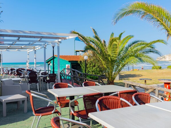 An outdoor seating area with tables and chairs, a small building, and a view of the ocean.