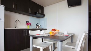 Une cuisine compacte avec des meubles de couleur sombre, un évier en acier inoxydable, une bouilloire et un panier de fruits posé sur le plan de travail.