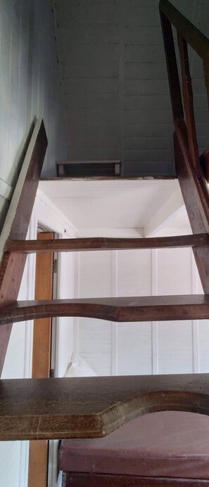 A wooden staircase leading to a room with white walls and a visible door. - Camburi Chalés (São Sebastião)