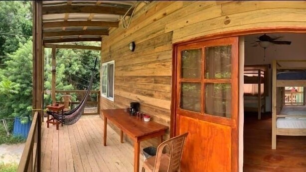 Una cabaña de madera con un porche, comedor y un dormitorio con literas.
