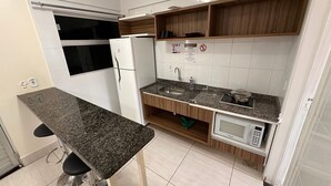 A compact kitchen with a granite countertop, a built-in microwave, a sink, and wooden cabinets. - Lacqua diRoma RM Hospedagem  (Caldas Novas)