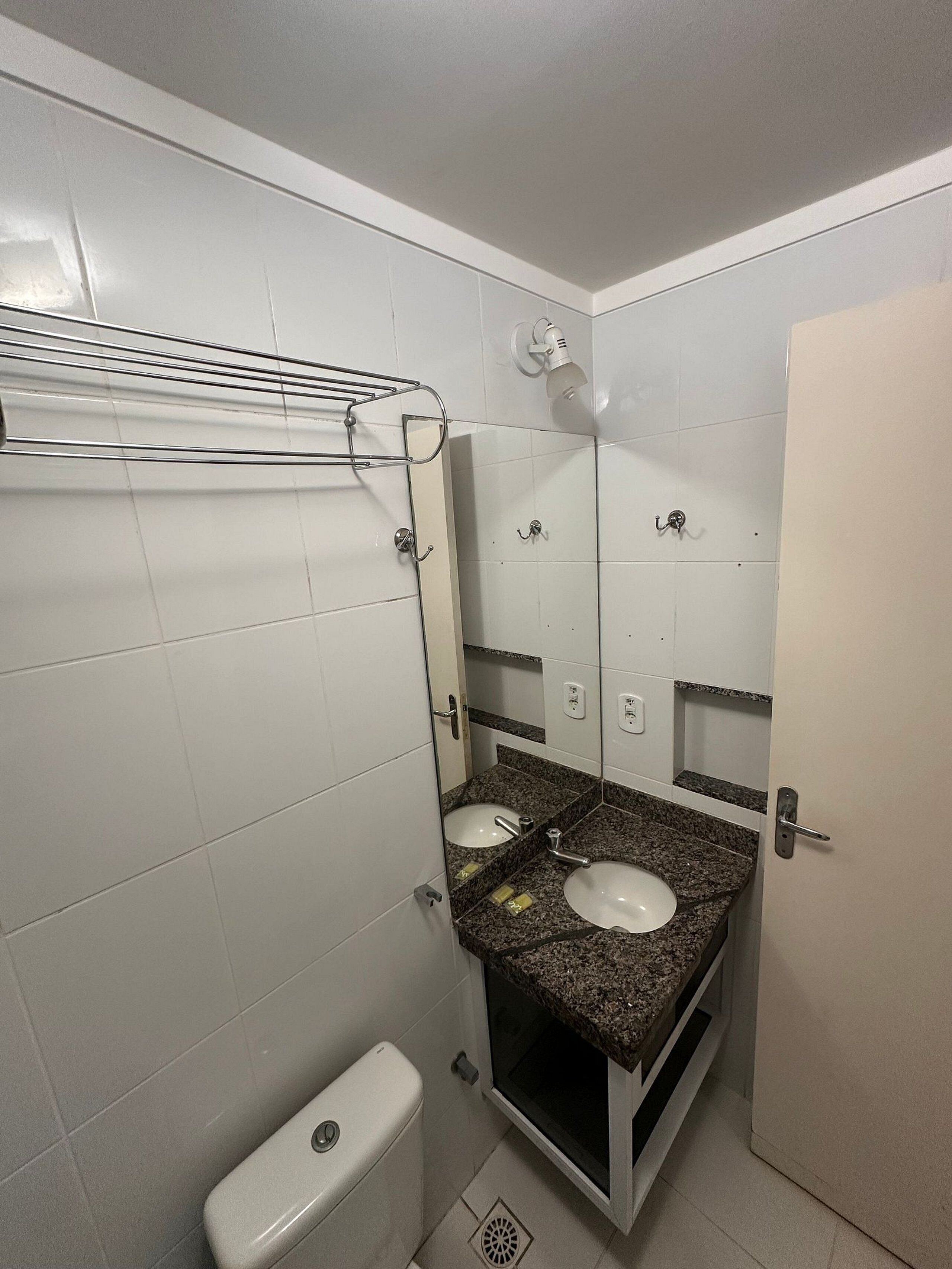 A small bathroom with white tiles, a sink, a toilet, and a shower.