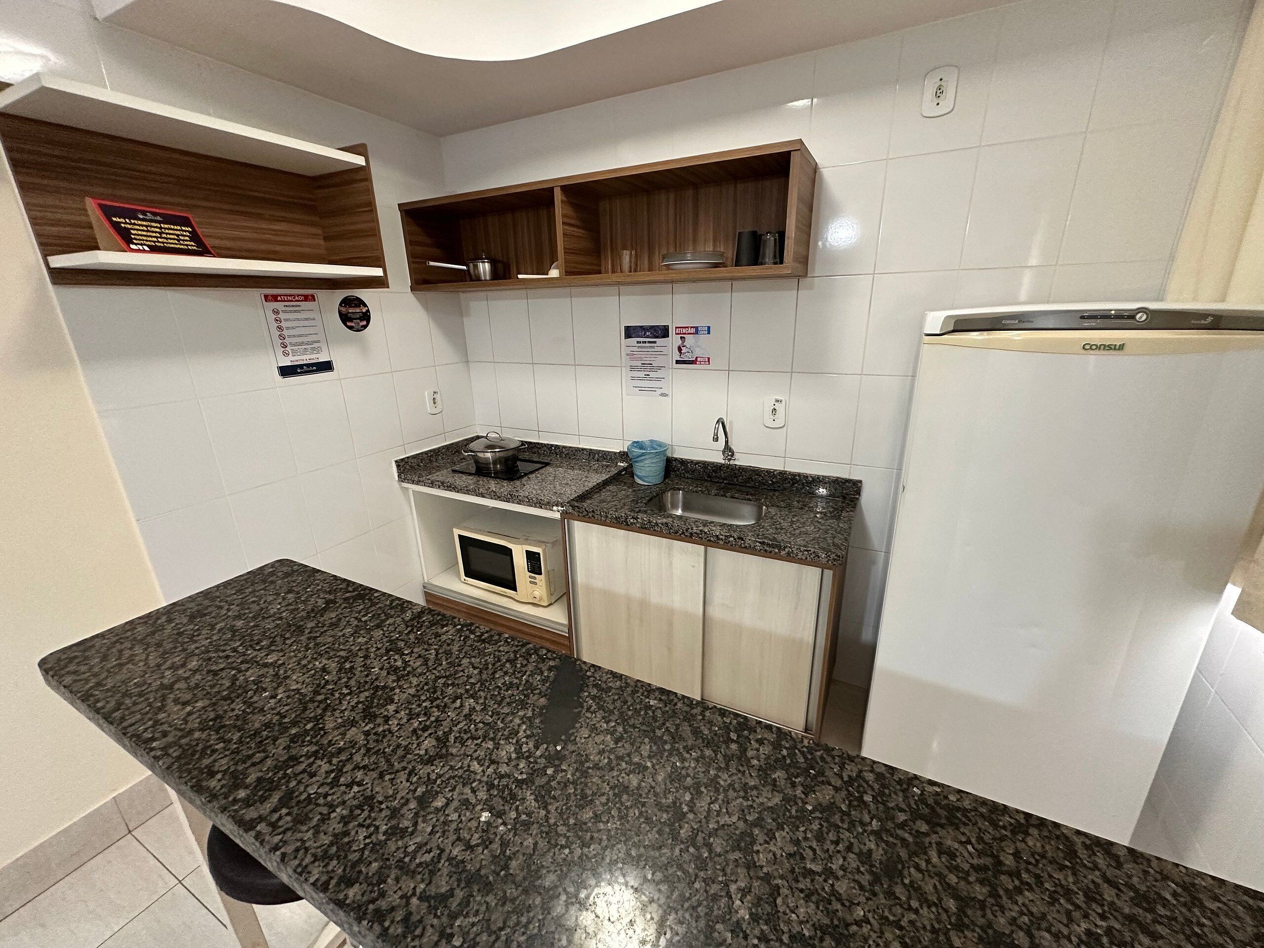 Een keuken met granieten aanrecht, een magnetron, een spoelbak en een koelkast.
