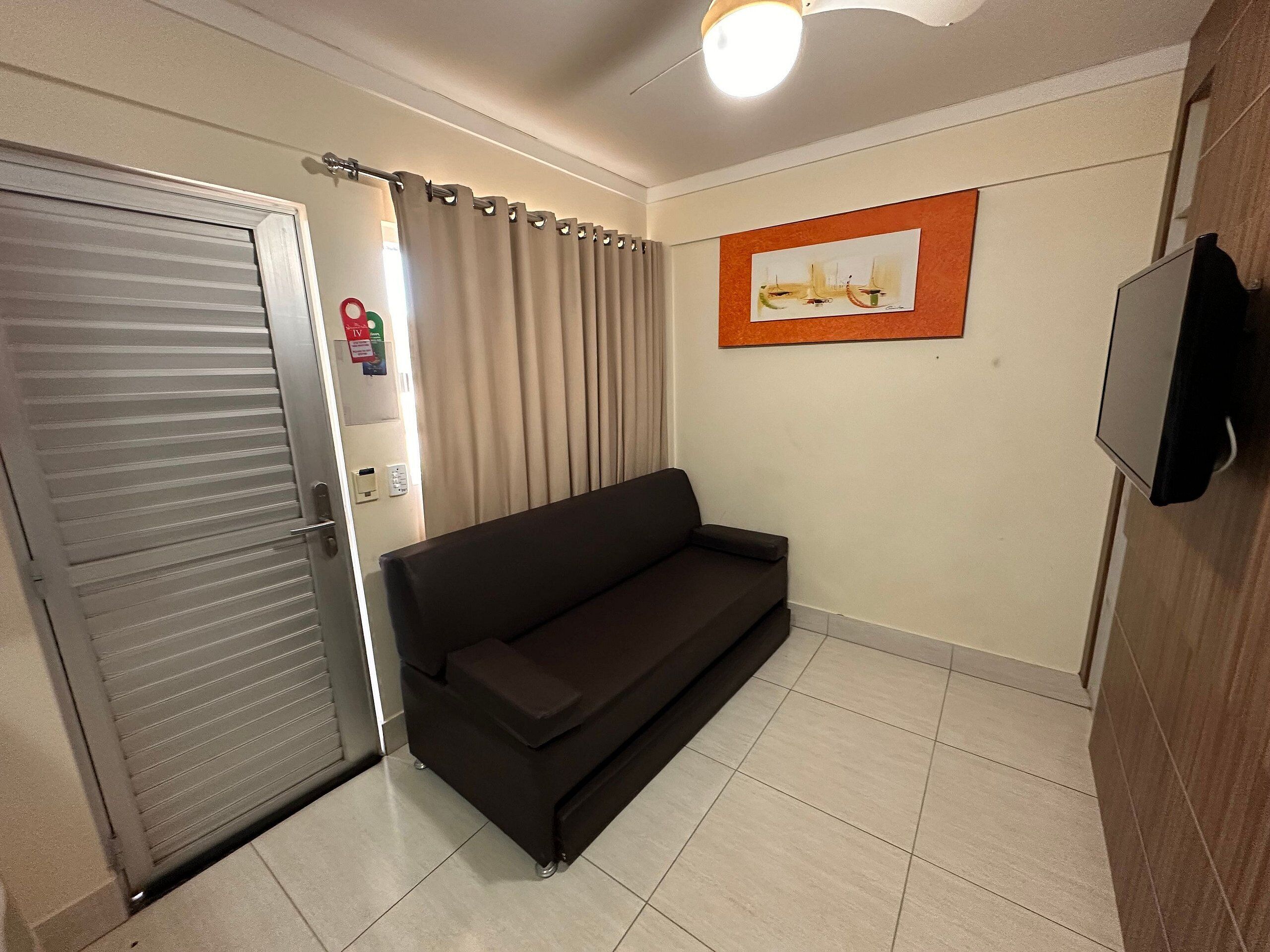 A room with a closed sliding door, a black sofa, a framed artwork on the wall, and a television mounted on the wall.