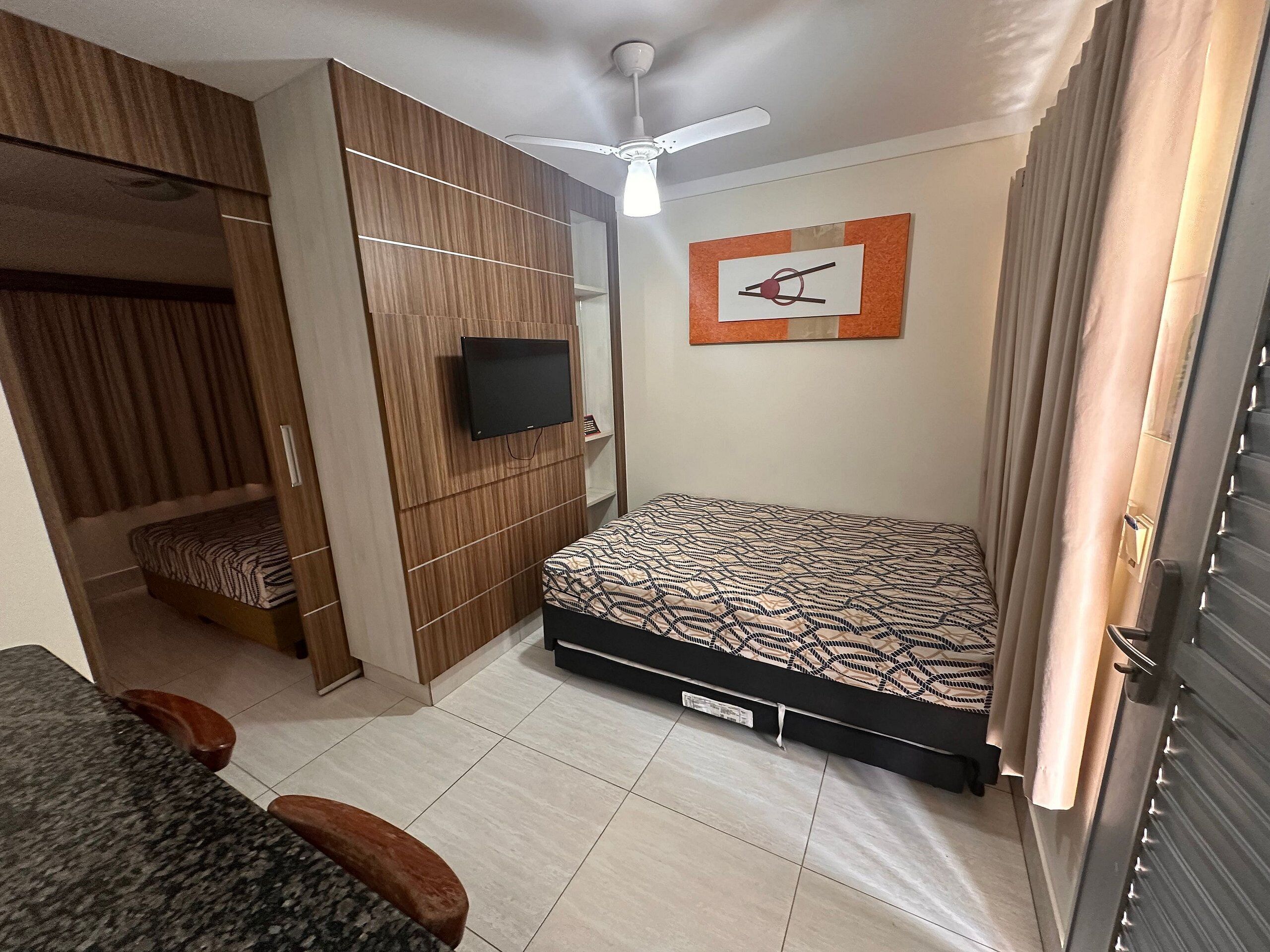 Un dormitorio con una cama, televisor, ventilador de techo y una obra de arte en la pared.