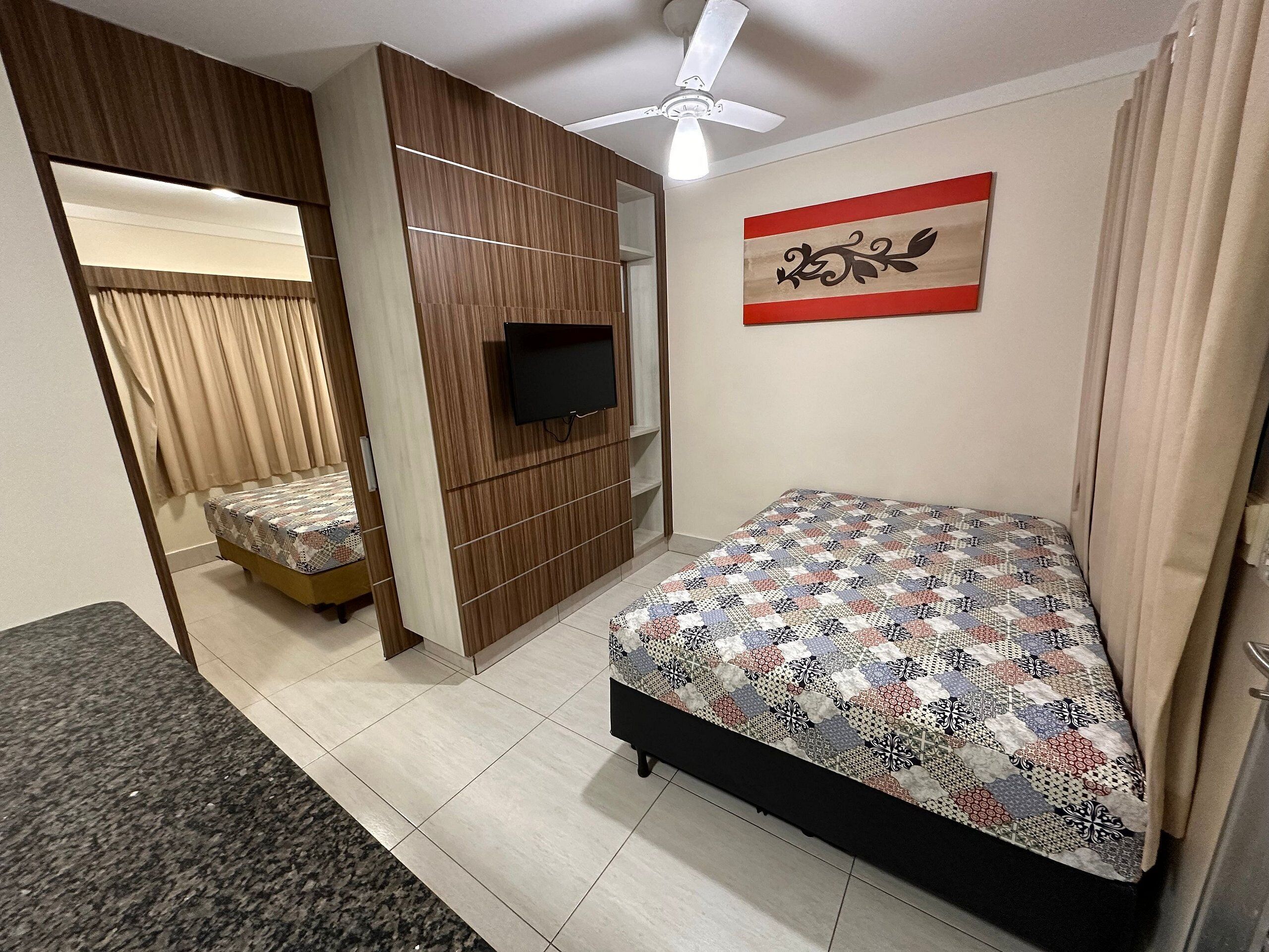 Une chambre à coucher comprenant un lit, un téléviseur, un ventilateur de plafond et un élément décoratif mural.