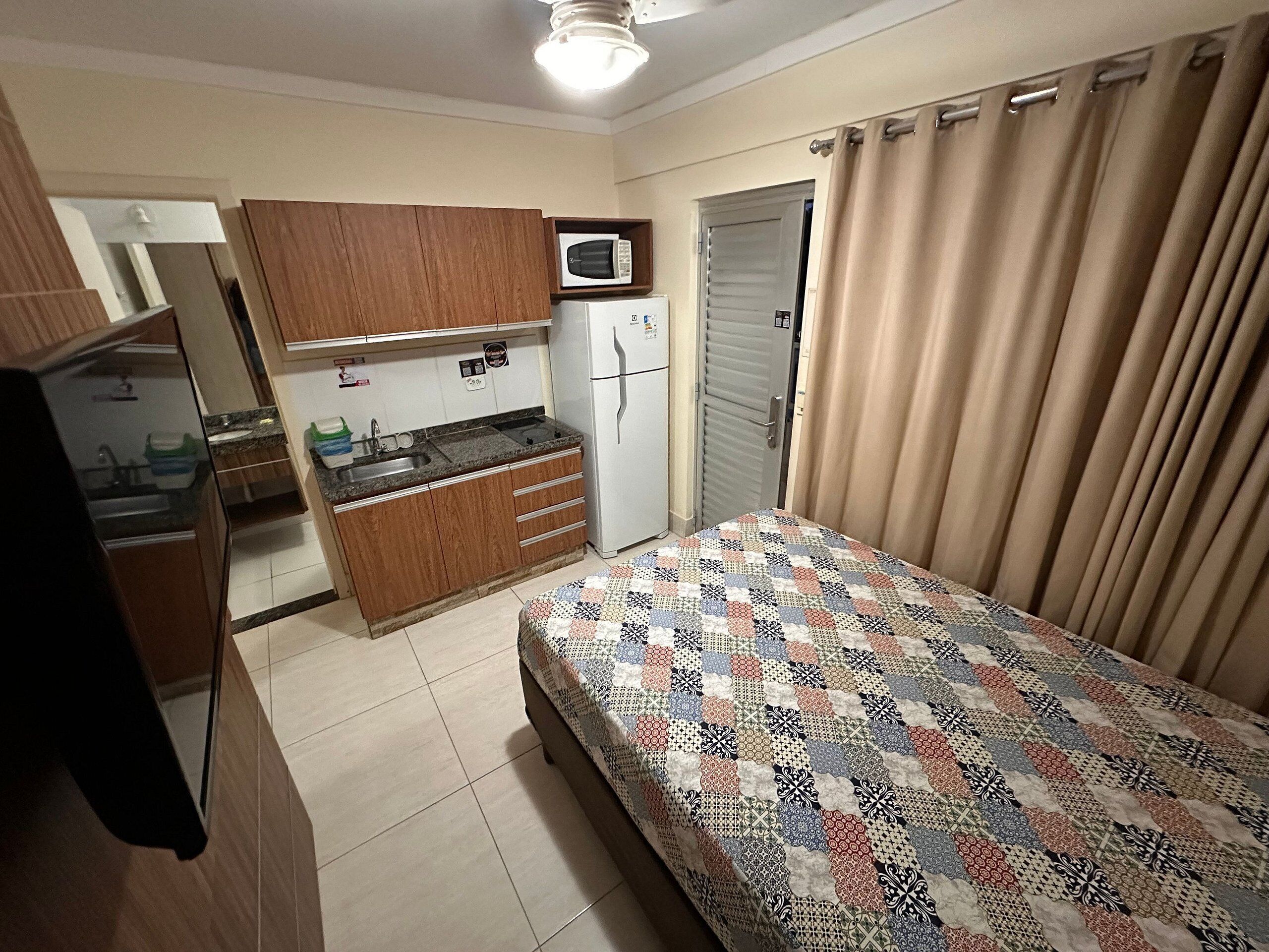 A compact room with a bed, kitchenette, and a door.