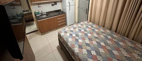 A compact room with a bed, kitchenette, and a door.
