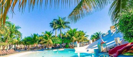 Una piscina con sillones de descanso y palmeras, rodeada de instalaciones turísticas.