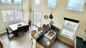 A modern kitchen with a large island, a dining area with a table and chairs, and multiple windows offering views of the city. - Hidden Pearl - City Skyline View - Free Hot Spa (Pittsburgh)