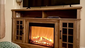 A living room with a fireplace, a flat-screen TV mounted above it, and a knitted throw on the floor. - Hidden Pearl - City Skyline View - Free Hot Spa (Pittsburgh)