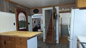 Une cuisine avec des meubles en bois, un îlot central, un réfrigérateur et un escalier menant à une autre pièce.