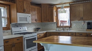 Une cuisine avec des meubles de rangement en bois, une cuisinière blanche, un four à micro-ondes et un plan de travail en bois.