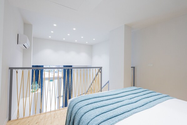 Un dormitorio moderno con una cama, piso de madera, una escalera y vistas al exterior.