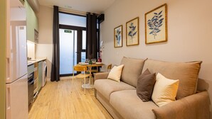 A compact living space with a kitchenette, a sofa with cushions, a dining table, and two framed botanical prints on the wall. - Olive Loft I | AC and WIFI | 10 min City Center (Valencia)