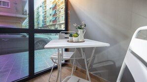 A small balcony with a white table and chairs, a potted plant, and a view of a cityscape through a large window. - Olive Loft I | AC and WIFI | 10 min City Center (Valencia)