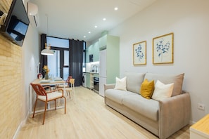 A modern living room with a sofa, a dining table with chairs, a kitchen area, and artwork on the walls.