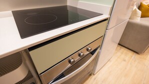 Et køkken med moderne induktionskogeblad, en rustfris stål ovn og et beige skab.