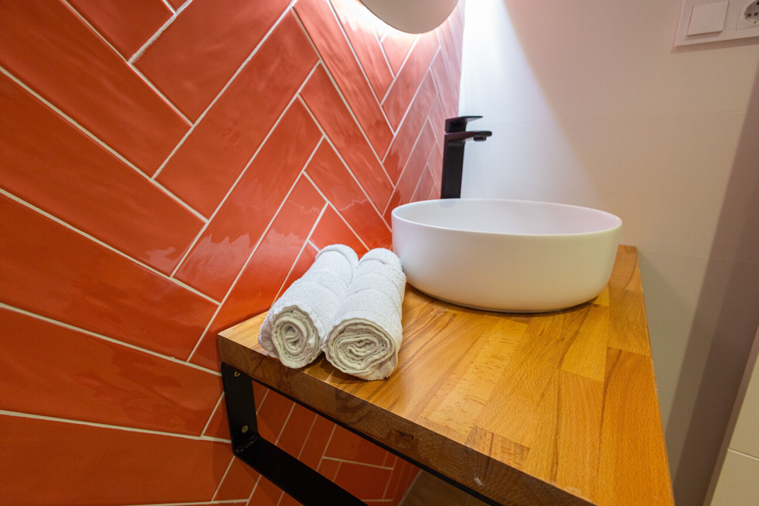 A bathroom with a wooden countertop, a white sink, and a towel rack holding two rolled towels.